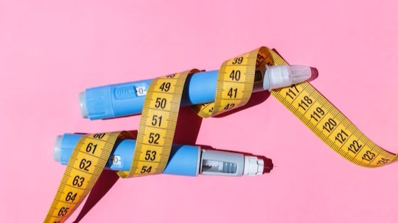 Tirzepatid - Zdravé potraviny na chudnutie a do jedálnička na mieru Two blue insulin pens wrapped with a yellow measuring tape against a pink background